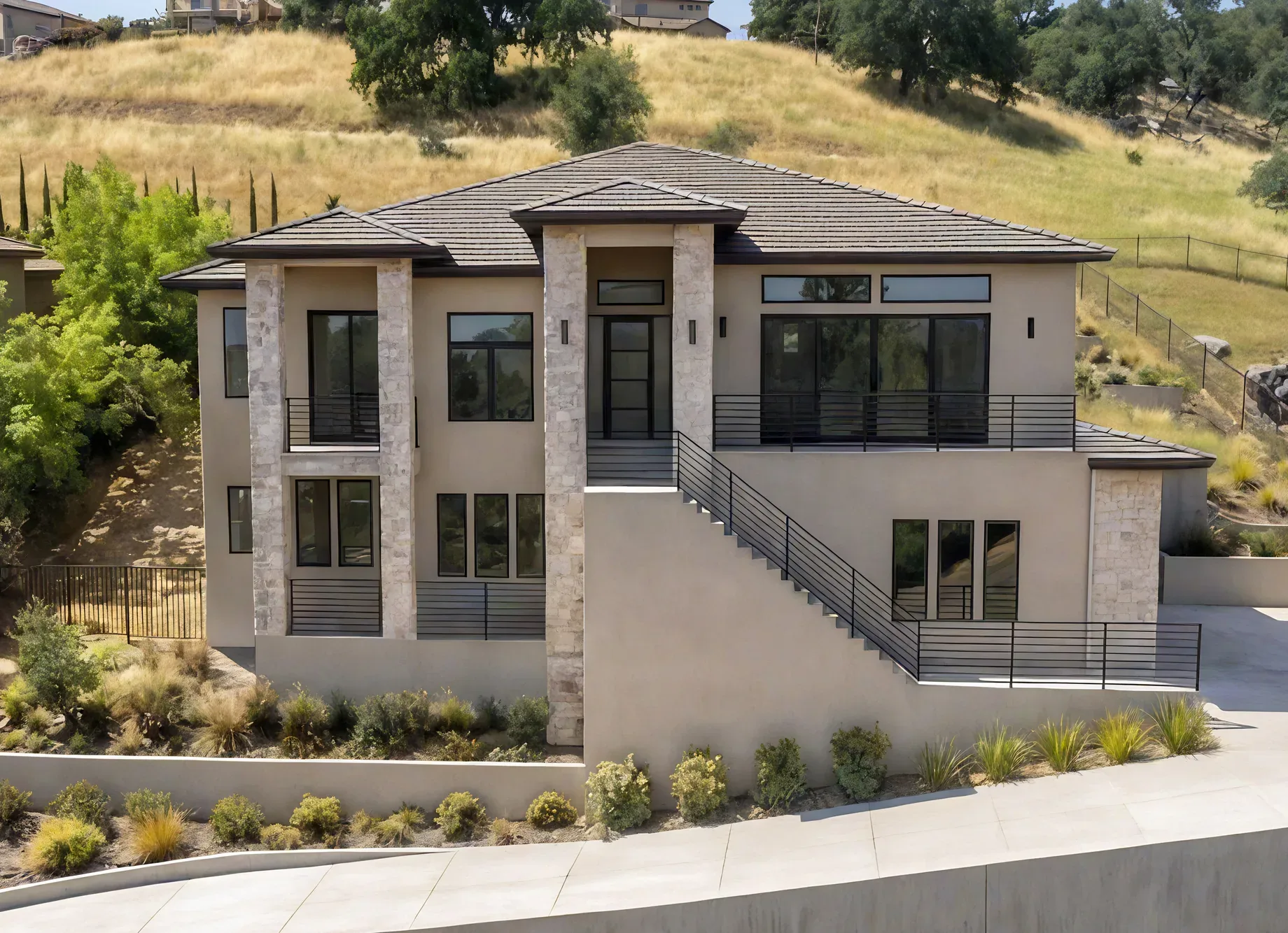 The same elevation as conceived: stone columns, warm stucco, steel railings, and a finished stair to the entry above a planted retaining wall