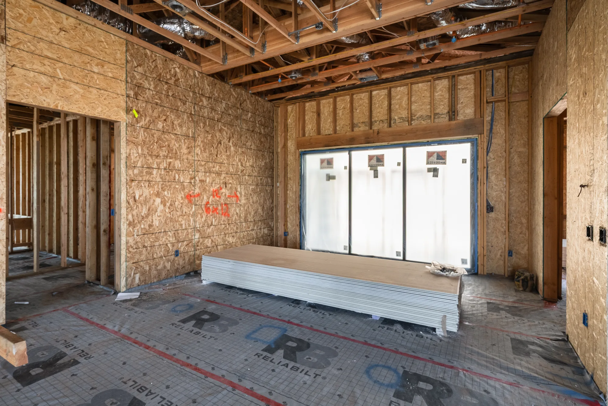 The dining room at framing stage: OSB sheathing, exposed trusses, and a wide slider opening sheeted over against the weather