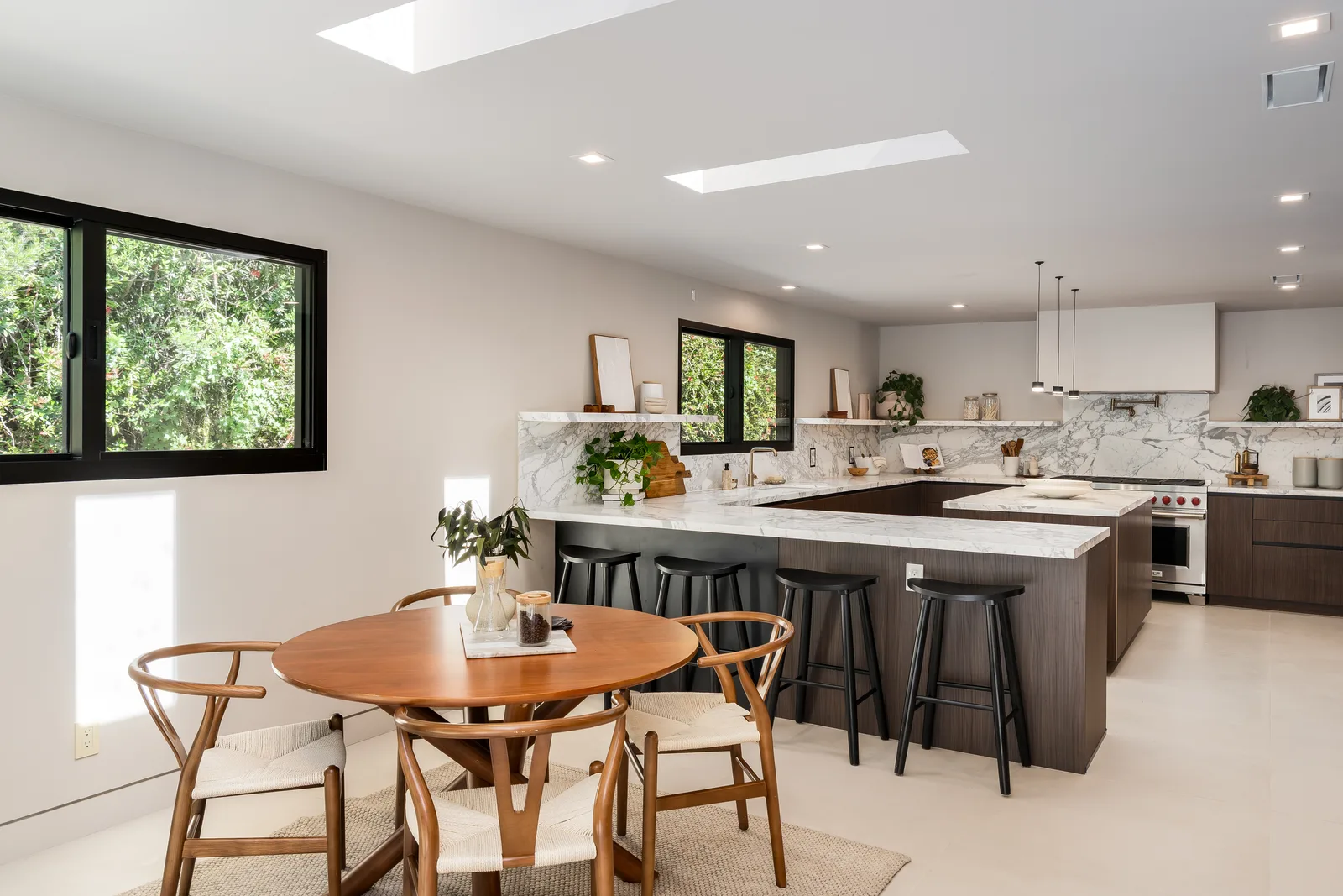 The kitchen at 5645 Bacon Road: marble waterfall counters, walnut cabinetry, and a breakfast table under the skylit spine