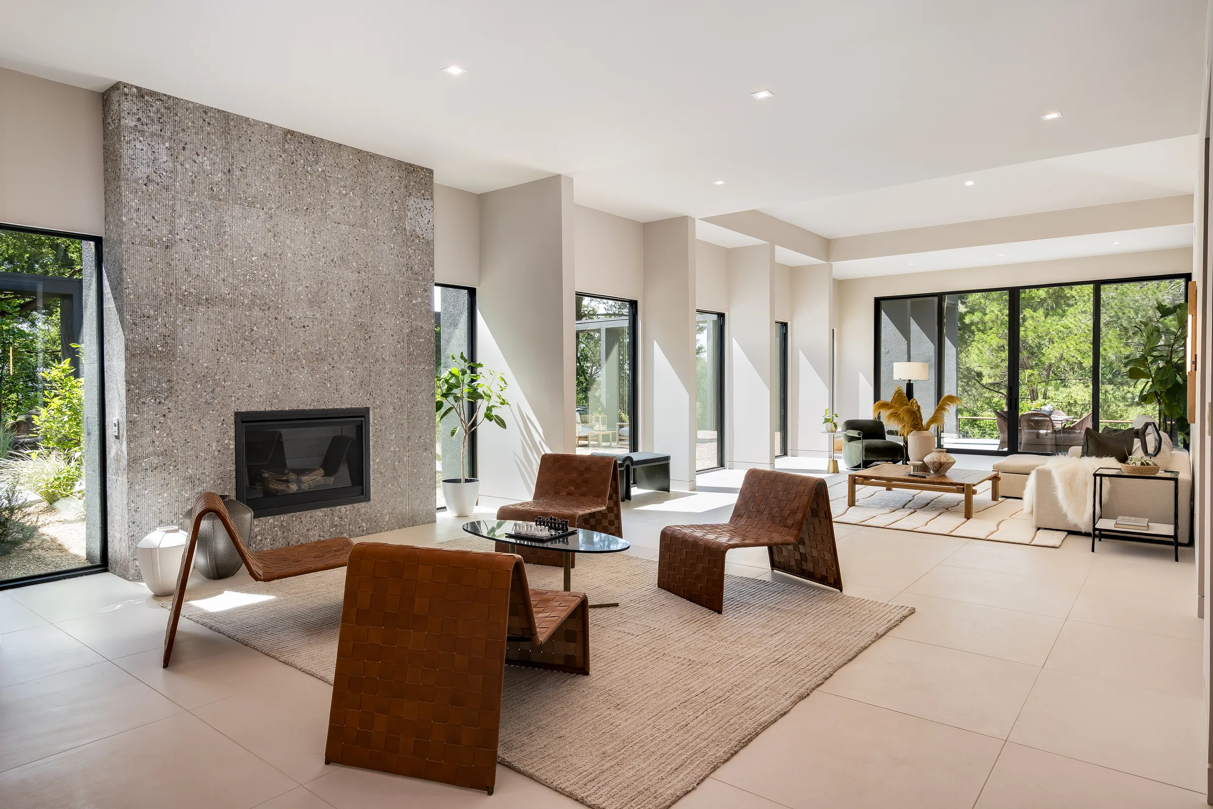 The great room at 5645 Bacon Road: the rebuilt aggregate-concrete fireplace anchoring a long, skylit spine of glass bays
