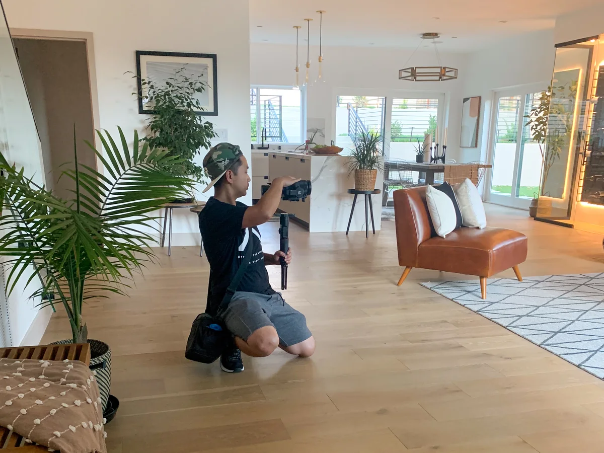 Mike kneeling with a camera in a staged living room, directing the shot.