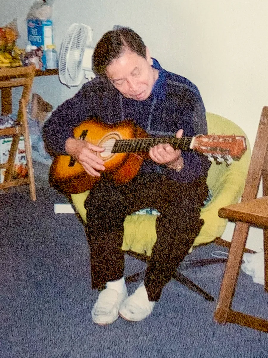Rachel's dad playing guitar in a folding chair, from a family print.