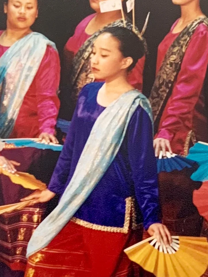 Rachel in blue at the front of a Filipino folk dance group, fan in hand, the dancers behind her in red and gold.